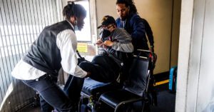 Two airline attendants lifting a person from a wheelchair to an airline seat