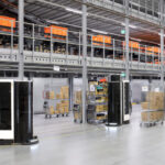 A warehouse with mobile robots and human workers moving items and carts.