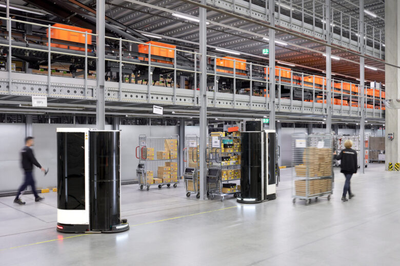 A warehouse with mobile robots and human workers moving items and carts.